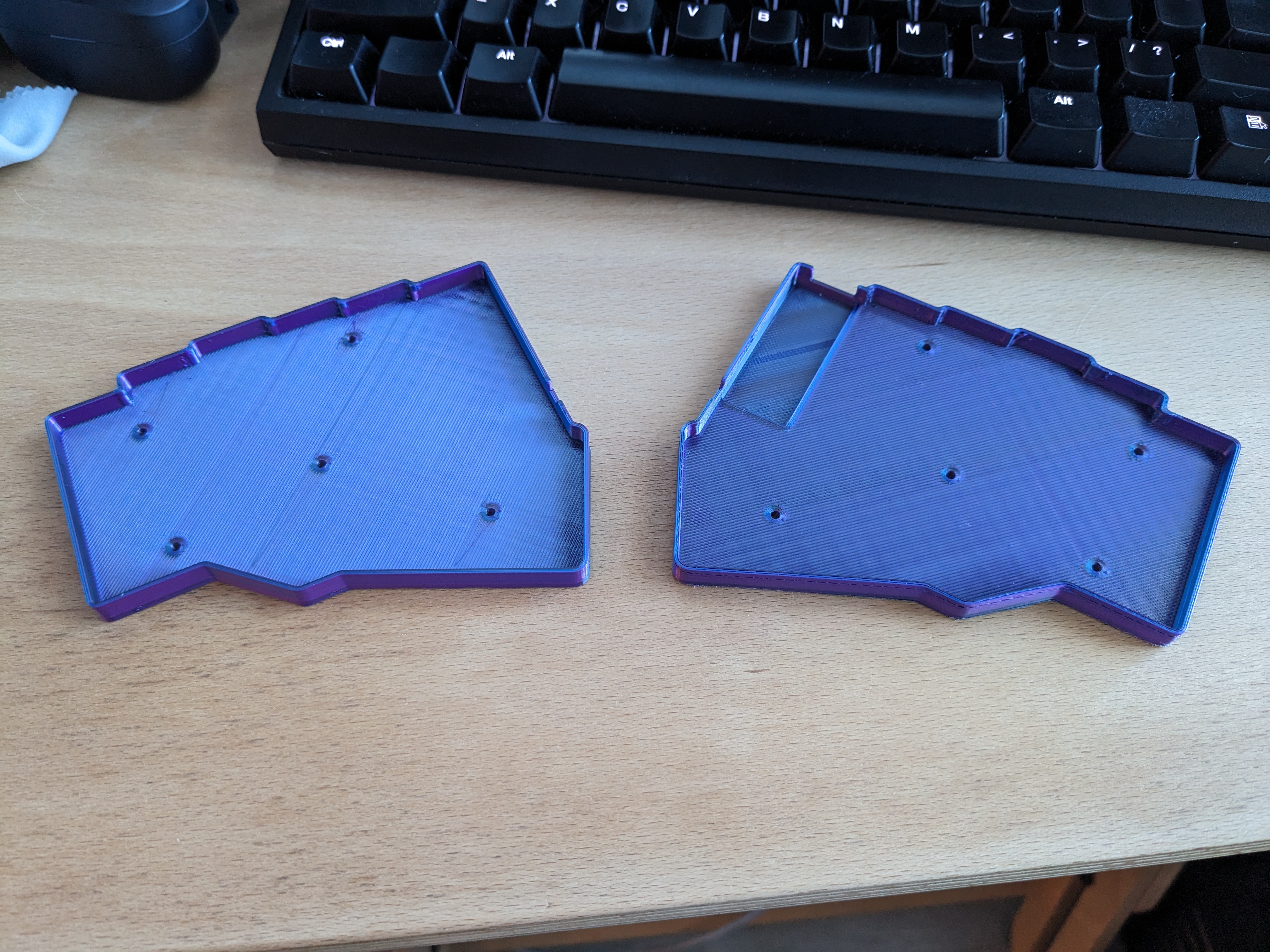 Two halves of an ergonomic split keyboard case, 3D-printed using a shiny blue, purple, and red filament